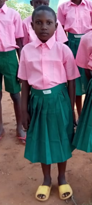 Ein Mädchen in einem pinken Hemd und grünem Rock steht neben anderen Kindern.