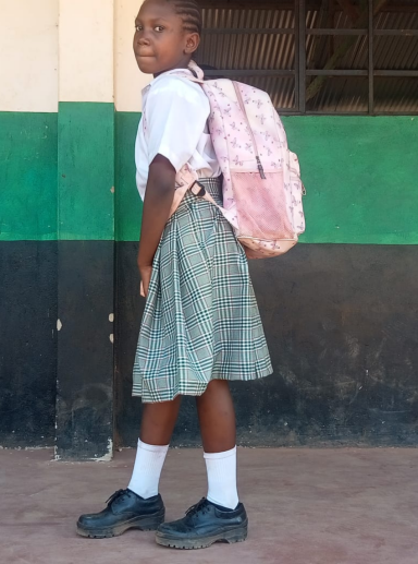 Ein Kind in Schuluniform mit Rucksack, steht vor einer farbigen Wand.