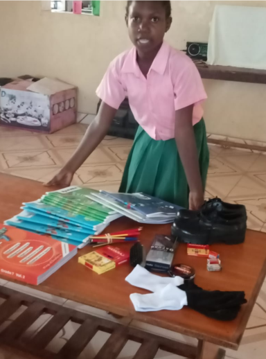 Ein Mädchen präsentiert Schulmaterialien und Kleidung auf einem Tisch.