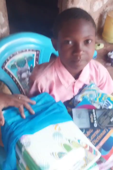 Ein lächelndes Kind sitzt auf einem Stuhl mit bunten Stoffen und Schulmaterialien.