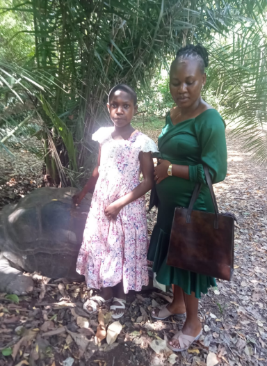 Eine Frau in grünem Kleid und ein Mädchen in rosa Kleid stehen im Freien zwischen Pflanzen.