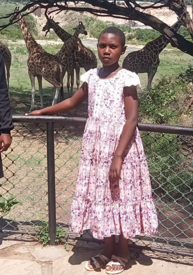 Mädchen in einem blumigen Kleid steht an einem Geländer mit Giraffen im Hintergrund.